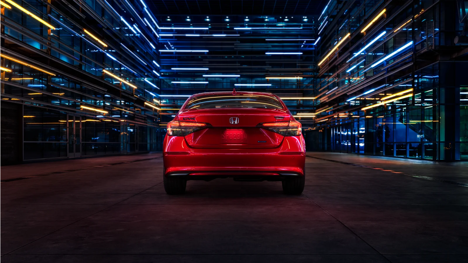 Rear view of a red Civic Sedan in a modern glass building lit with blue and amber light.