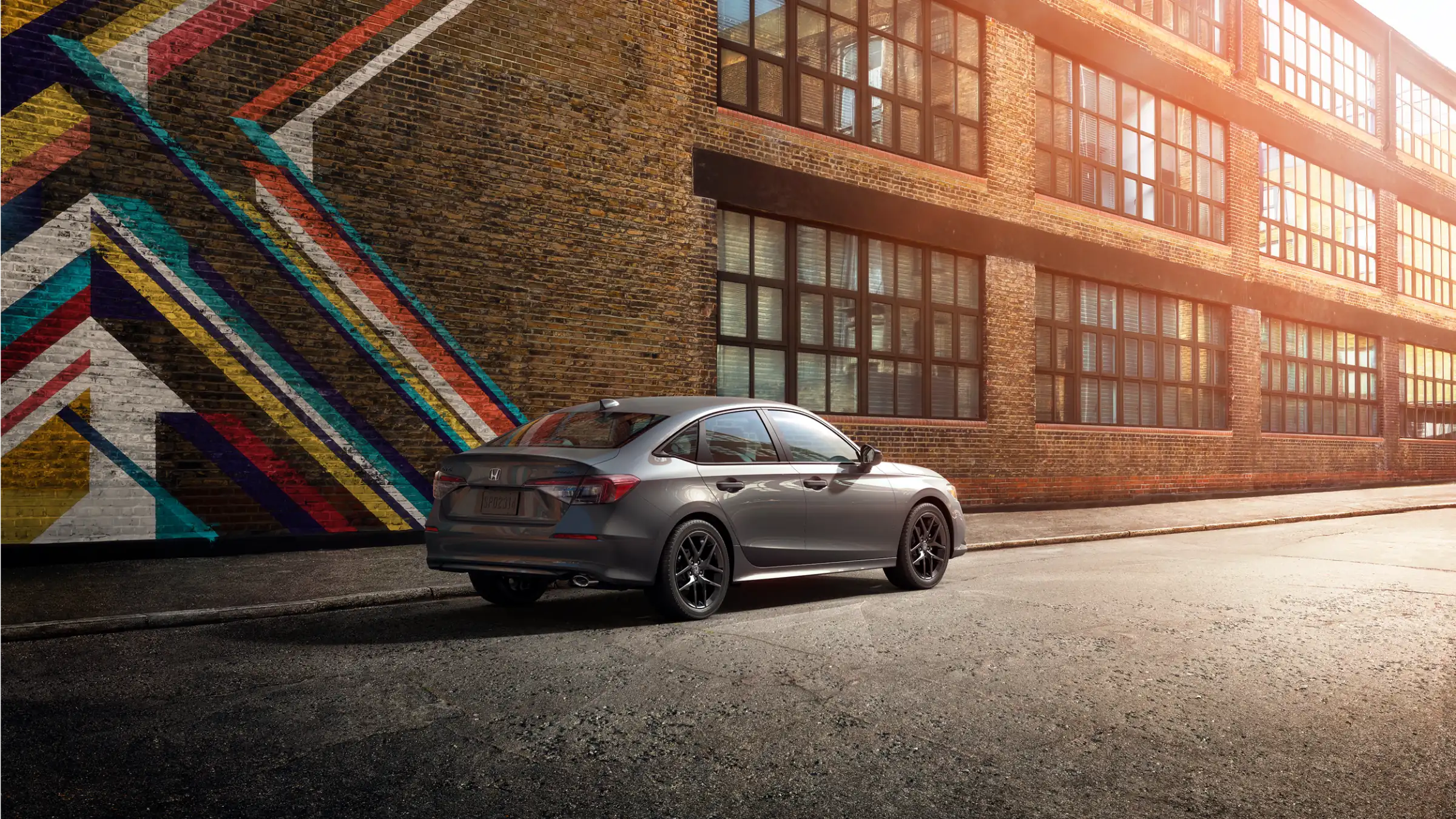 A grey Honda Civic Sedan parked beside a colourful mural on a brick building.