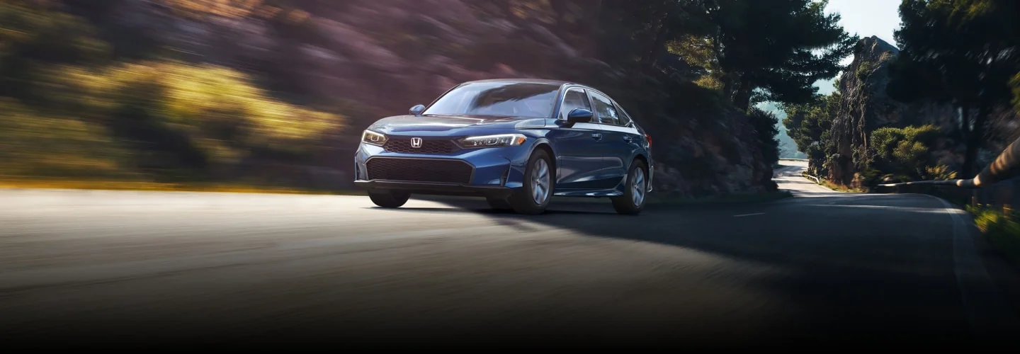 A blue Civic Sedan driving on a sunny, tree-lined road.