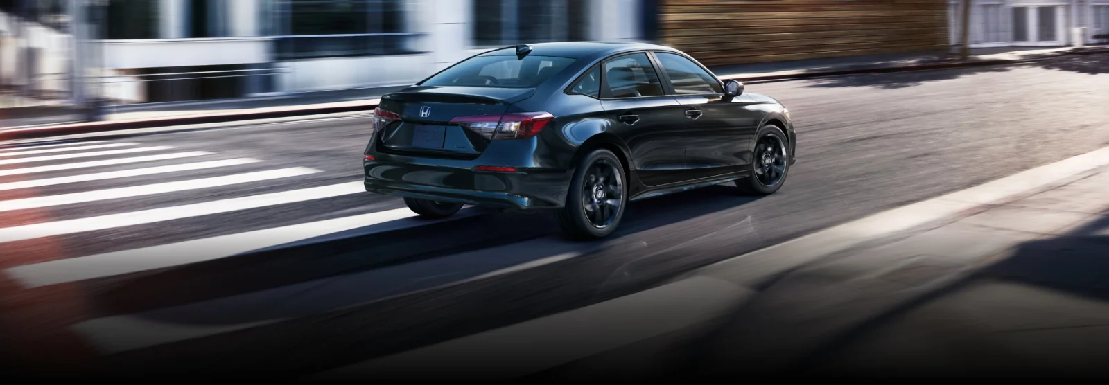 A black Civic Sedan driving through a city crosswalk.