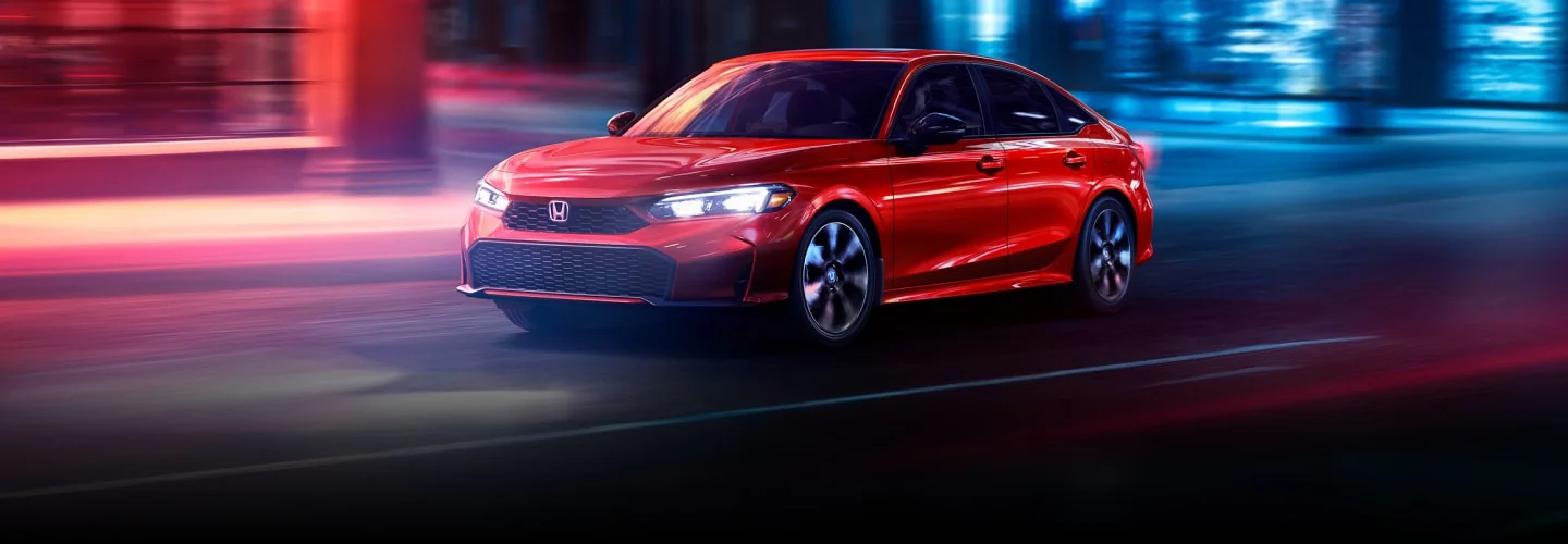 A red Civic Sedan driving through a city at night with streaks of light behind it.