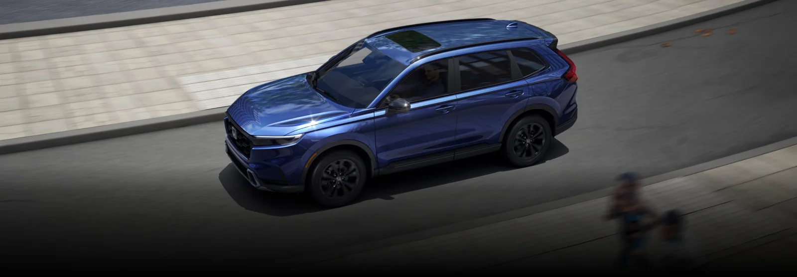A blue CR-V driving along a sunlit city street, seen from above.