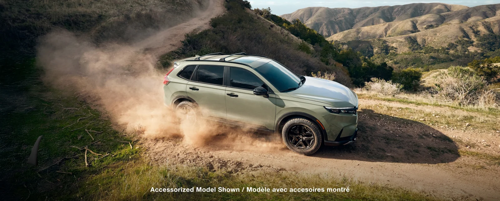 A green CR-V kicking up dust as it climbs a grassy hillside trail.