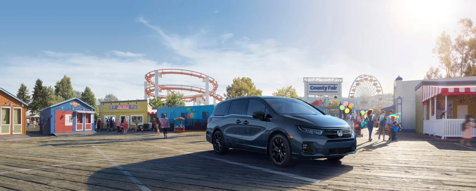 A dark grey Odyssey parked on the boardwalk at a summer county fair.