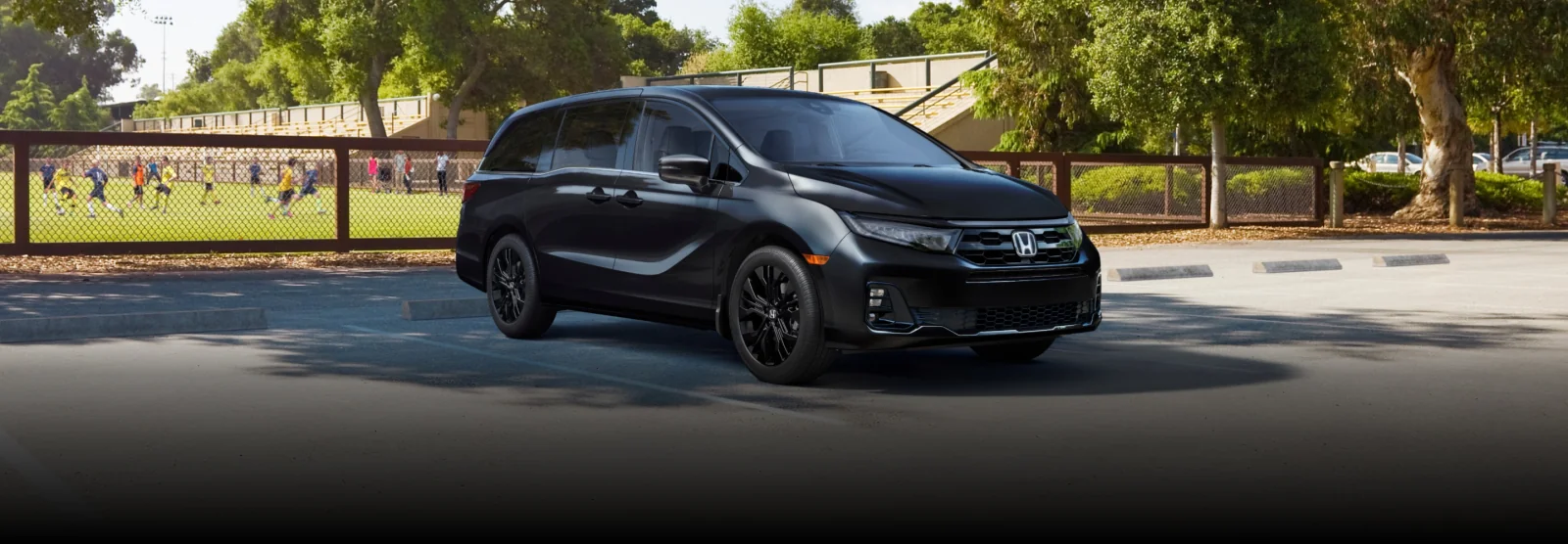 A black Odyssey parked beside a soccer field.