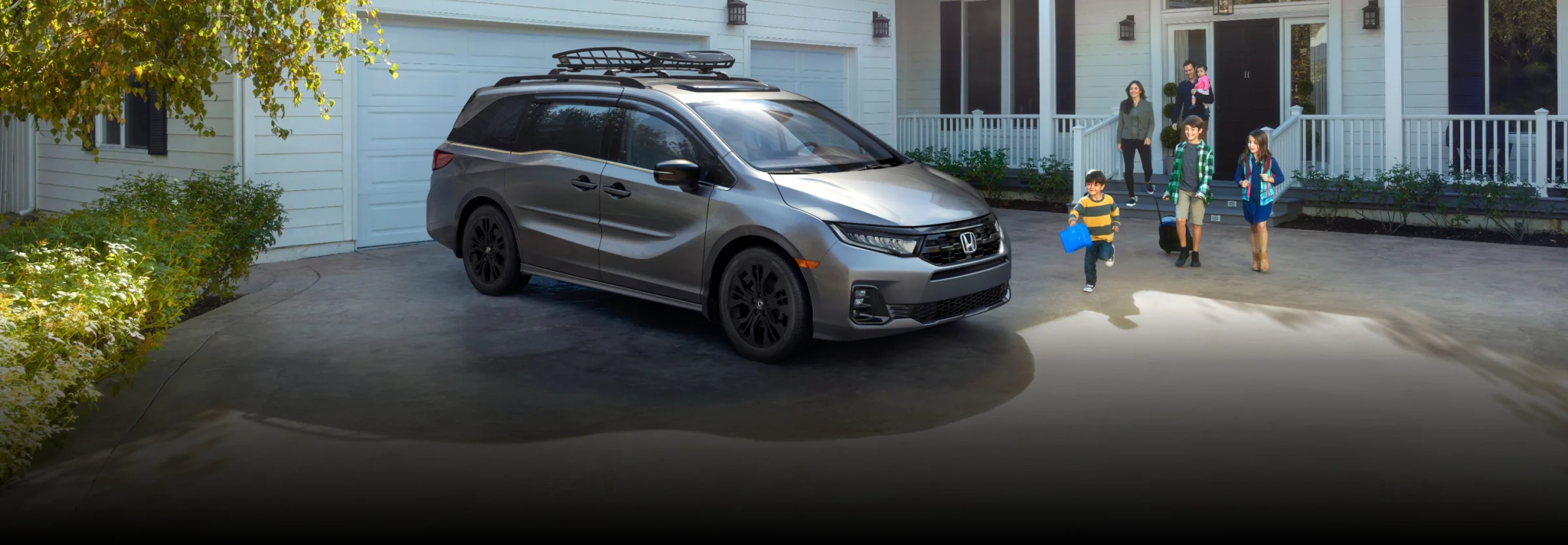 A grey Honda Odyssey in a driveway as a family heads out of the house toward it.