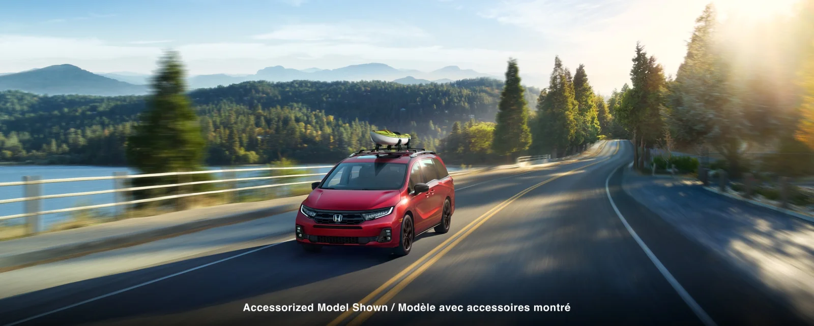 A red Odyssey with a roof-mounted cargo rack driving along a lakeside road.