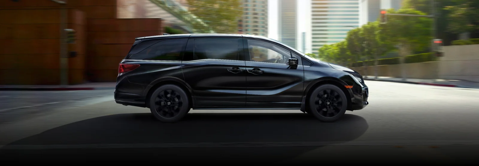 Side view of a black Odyssey driving through a sunny downtown street.