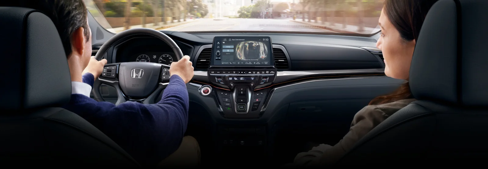 A driver and passenger in the front seats of an Odyssey with the centre touchscreen in view.