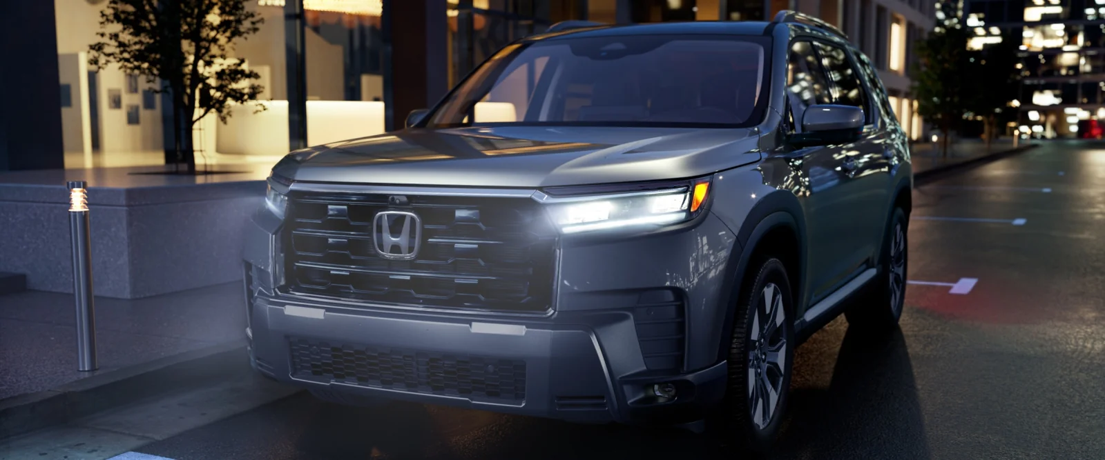 Front view of a silver Pilot with its LED headlights on, parked on a city street at dusk.
