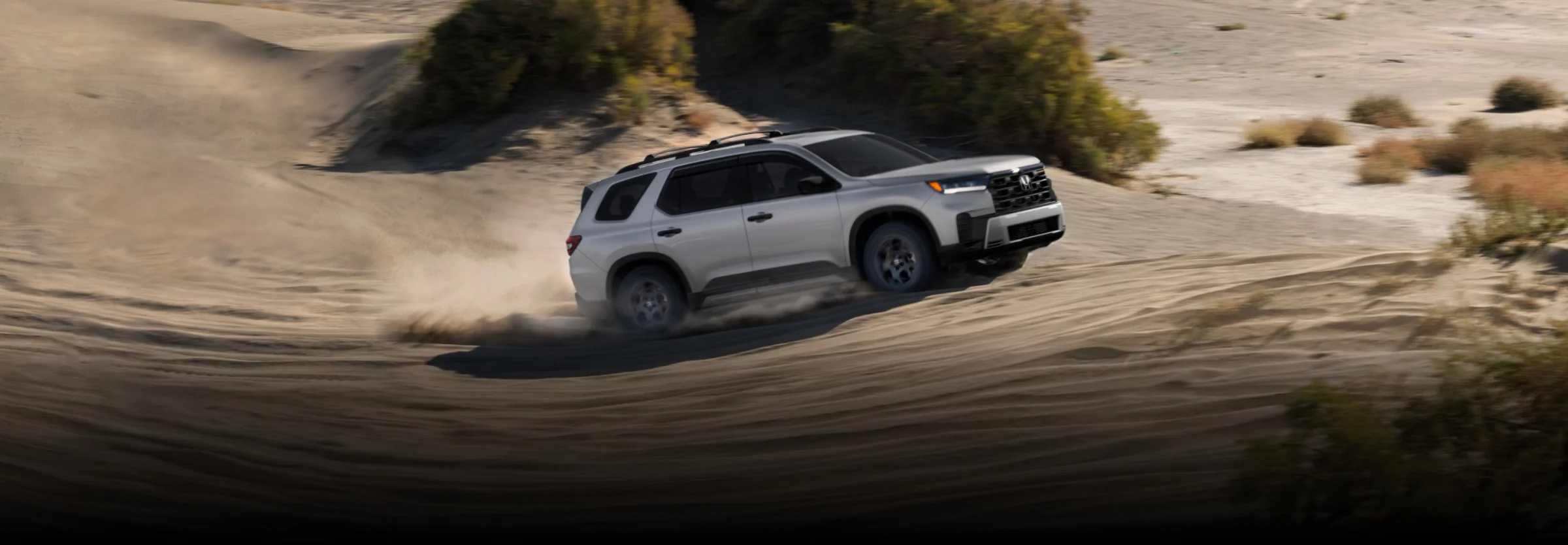 A white Honda Pilot powering through desert sand dunes.